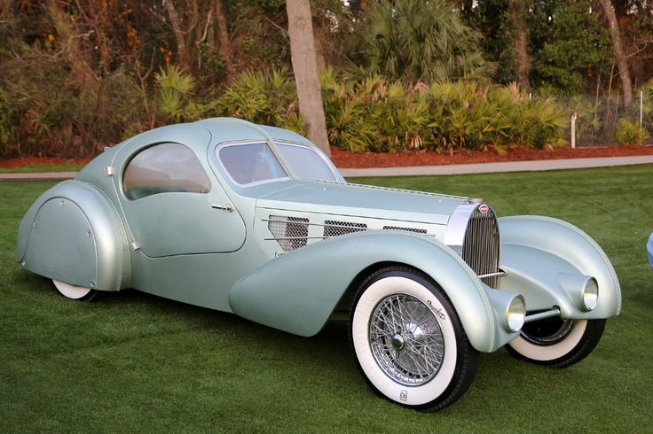 Bugatti Type 57 Aérolithe Wallpapers _ Supercars_net - Engine Stories Vintage luxury car, silver color, with classic design, displayed on grass with trees in the background at an outdoor auto show.