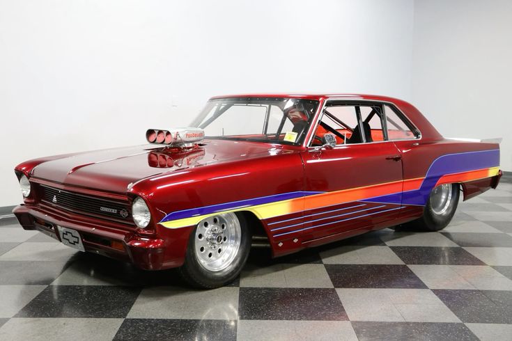 Chevy II - Engine Stories Red vintage Chevrolet drag race car with colorful detailing and modified engine, showcased in a bright showroom.