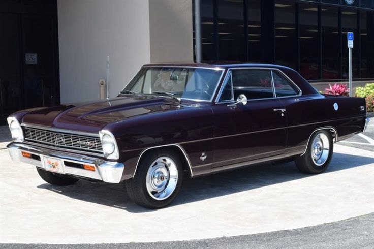 Chevy Nova - Engine Stories Vintage purple classic car parked outside a modern building on a sunny day.
