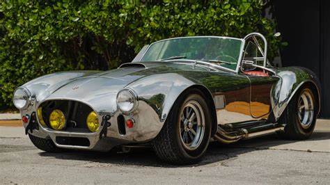 Cobra II Special 1966 - Engine Stories Vintage silver sports car with open-top, parked outdoors, showcasing classic design and shiny exterior.