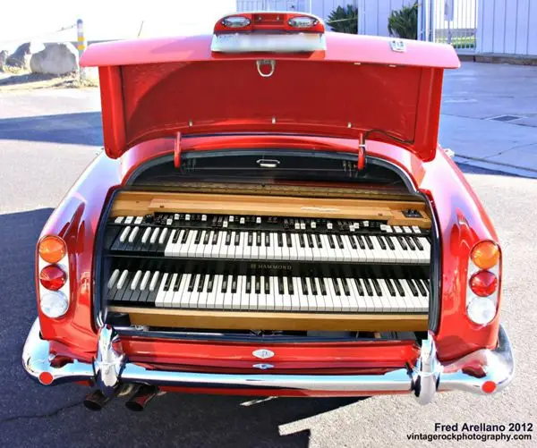 Vintage red car with trunk open, revealing a Hammond organ inside. Creative musical twist on classic automotive design.