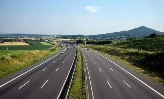 Open highway with clear skies, surrounded by green fields and distant hills, illustrating tranquil driving conditions.