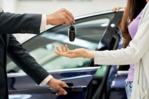 Car keys being handed over, symbolizing a new car purchase or lease. Blue car in background. Buying a car concept.