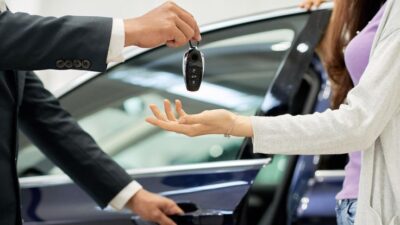 Car keys being handed over, symbolizing a new car purchase or lease. Blue car in background. Buying a car concept.