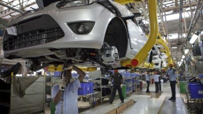 Car assembly line with workers installing components on a silver car. Industrial manufacturing process in an automotive factory.