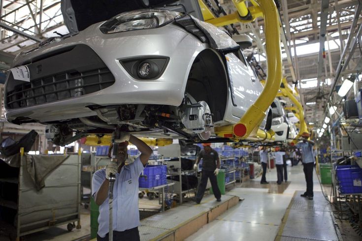 Car assembly line with workers installing components on a silver car. Industrial manufacturing process in an automotive factory.