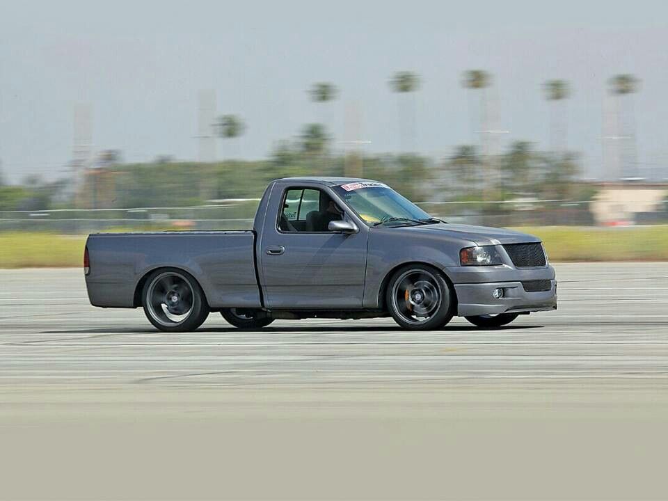 Fords Stealth Fighter 1972 - Engine Stories Lowered gray pickup truck driving on a sunny day, blurred palm trees in the background, showcasing speed and performance.