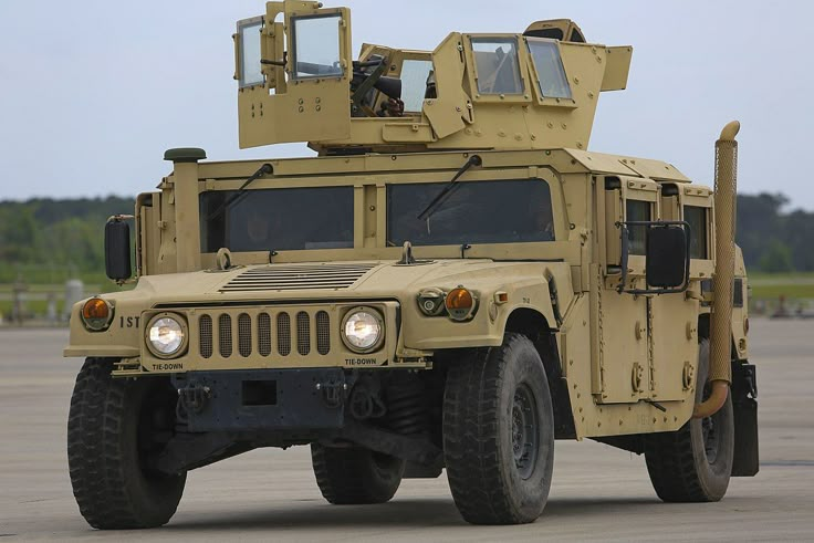 Military armored vehicle parked on an open field, front view showing rugged design and armored turret against a clear sky.