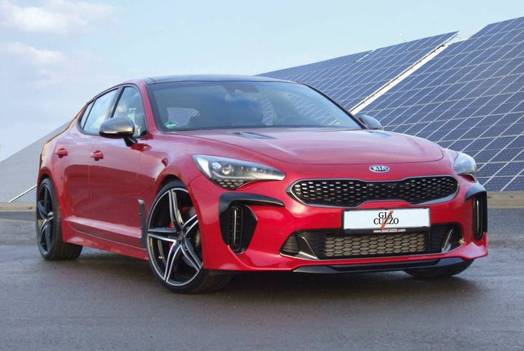 Red Kia Stinger parked in front of solar panels, showcasing sleek design and eco-friendly backdrop.