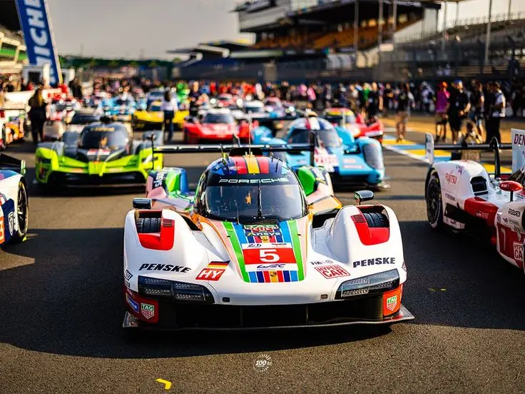 Racing cars lined up on a track, vibrant liveries under the sun, preparing for a competitive motorsport event.