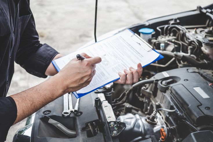 Mechanic conducting a car inspection with a checklist, ensuring vehicle safety and maintenance under the hood.