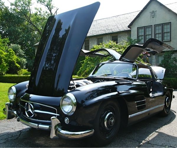 Classic black Mercedes with gullwing doors open, parked in front of a house. Perfect luxury car for enthusiasts.