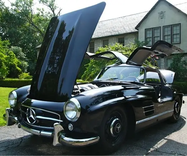 Mystery History_ 1954 Mercedes 300SL Gullwing - Engine Stories Classic black Mercedes with gullwing doors open, parked in front of a house. Perfect luxury car for enthusiasts.