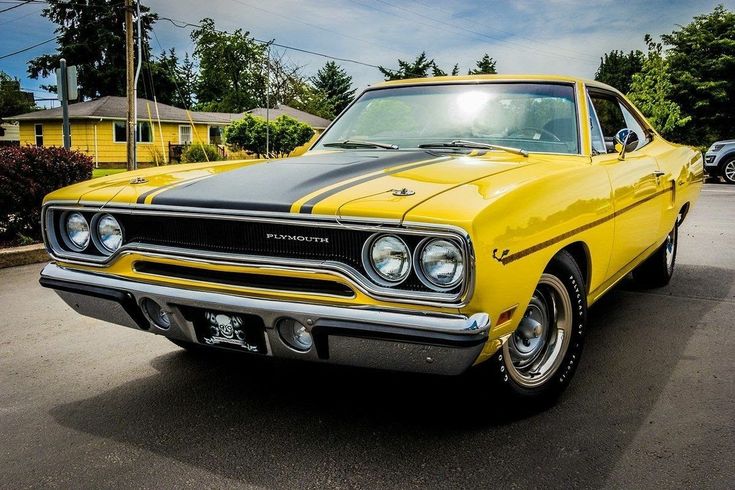 Yellow vintage Plymouth car with black racing stripes parked outdoors on a sunny day. Classic muscle car enthusiasts' favorite.