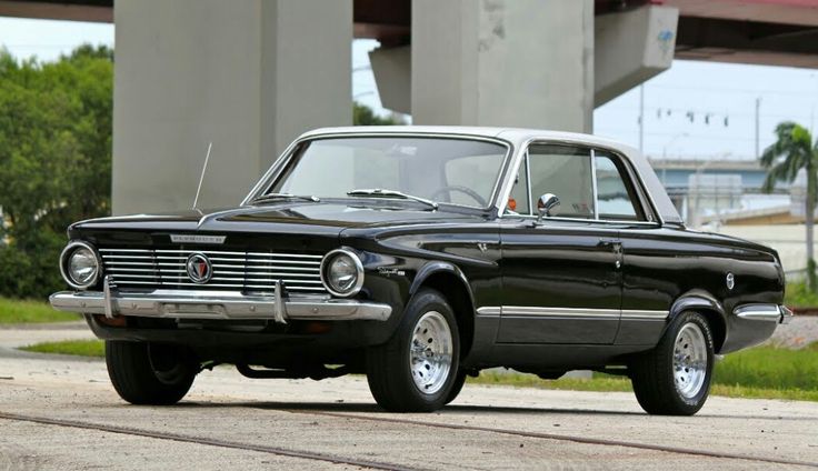 Plymouths Valiant 1964 - Engine Stories Classic black vintage car parked under a bridge with greenery in the background, showcasing retro design and style.
