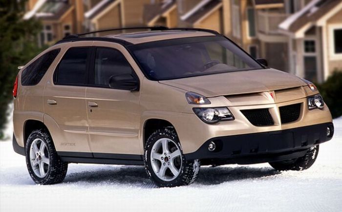 Pontiac Aztek_ The back end looks like an - Engine Stories Beige SUV on a snowy road in front of houses, showcasing robust design and winter readiness.