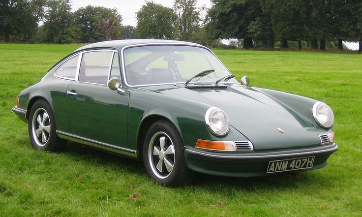 Classic green Porsche 911 parked on lush grass, surrounded by trees, showcasing vintage elegance and timeless design.