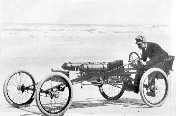 RansomEliOldsOldsPirate - Engine Stories Man in vintage open-wheel race car on a beach, showcasing early automotive design and innovation.