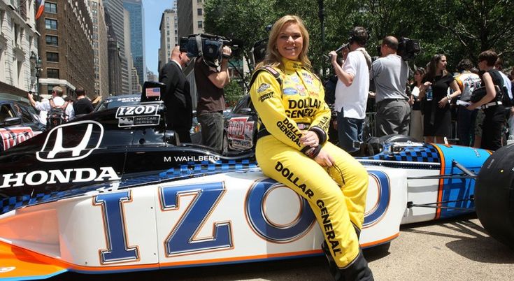 Sarah Fisher - Engine Stories Race car driver in yellow Dollar General suit poses by an IZOD Honda car on a bustling city street.
