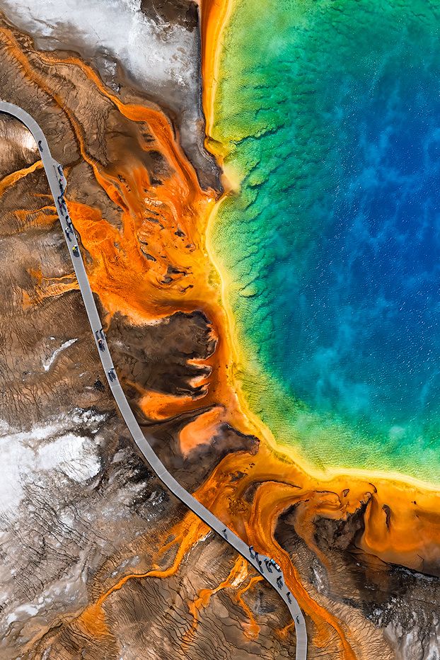 Aerial view of Yellowstone's Grand Prismatic Spring with vibrant blue, green, and orange colors, boardwalk, and tourists.