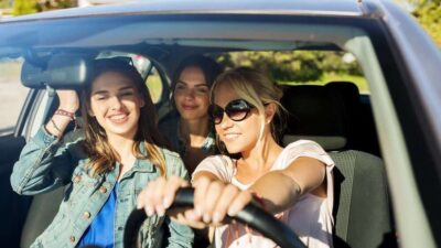 Group of friends in a car, smiling and enjoying a sunny road trip adventure together.