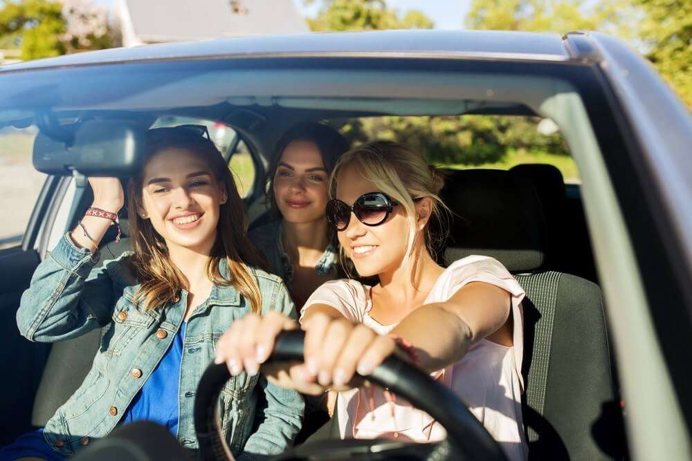 Group of friends in a car, smiling and enjoying a sunny road trip adventure together.