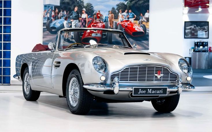 The Aston Martin DB5 1964 - Engine Stories Classic silver convertible Aston Martin displayed in luxurious showroom setting.