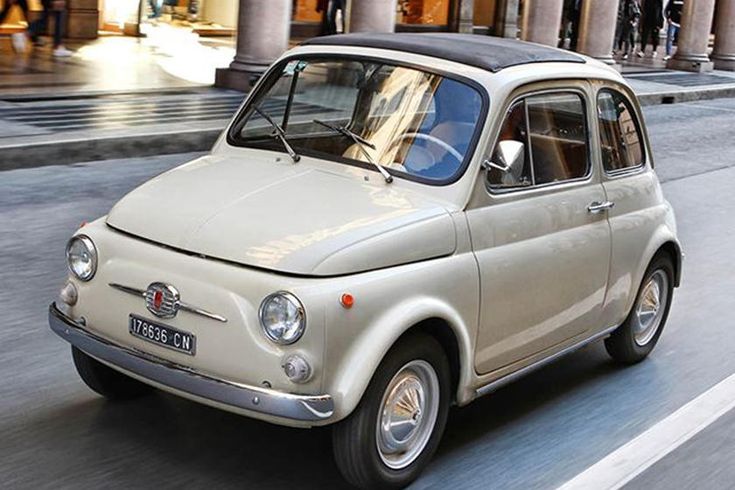 Vintage white car driving through city street, reminiscent of classic European design.