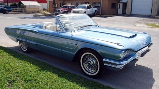 Thunderbird GT 1965 - Engine Stories Classic blue convertible car parked on a sunny day, showcasing its vintage design and whitewall tires.