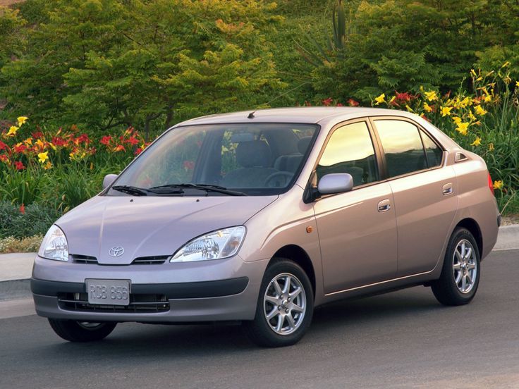 Silver sedan parked in front of lush green garden with colorful flowers on a sunny day.