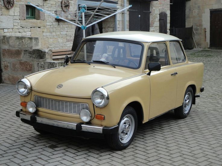 Trabant 1957 - Engine Stories Beige vintage car parked in a courtyard with cobblestone pavement, showcasing classic design and historical charm.