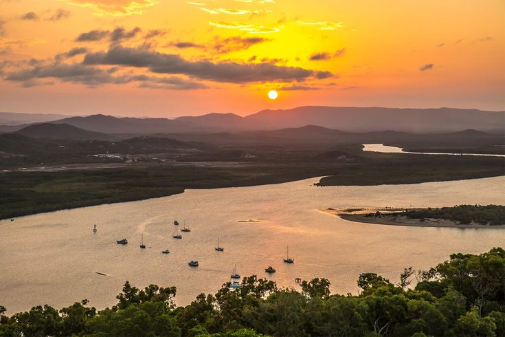 Sunset over a serene river with boats and lush greenery, creating a tranquil and picturesque landscape.