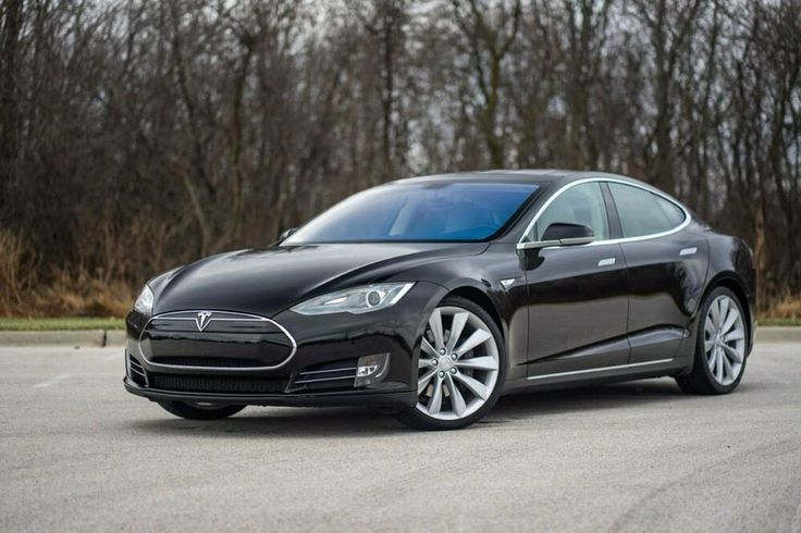 Used 2012 Tesla Model S For Sale - Engine Stories Sleek black electric car parked outdoors, featuring modern design and aerodynamic body, amidst a natural wooded backdrop.