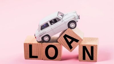 Toy car on wooden blocks spelling LOAN against pink background, symbolizing car loans and financing options.