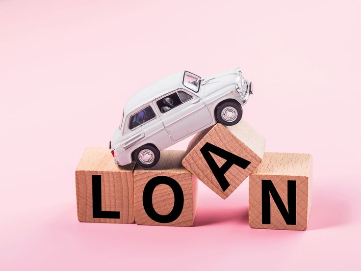 Toy car on wooden blocks spelling LOAN against pink background, symbolizing car loans and financing options.