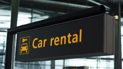 Car rental sign at an airport terminal, black background with yellow text, offering easy vehicle hire for travelers.