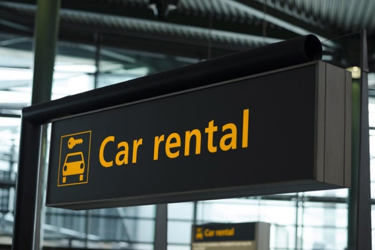 Car rental sign at an airport terminal, black background with yellow text, offering easy vehicle hire for travelers.