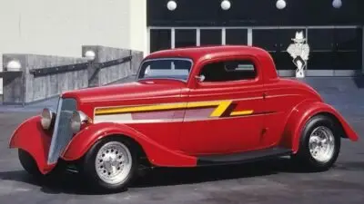 Red vintage hot rod with yellow stripes parked in an urban setting, showcasing classic design and polished chrome wheels.