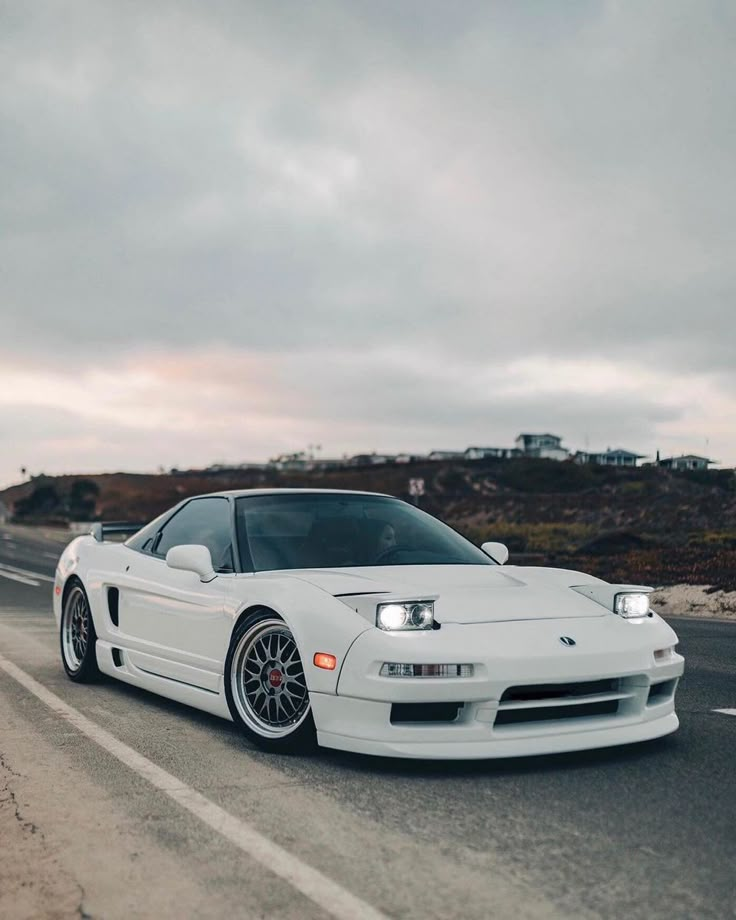 White sports car parked on scenic coastal road under cloudy sky. Classic design, sleek and stylish, perfect for car enthusiasts.