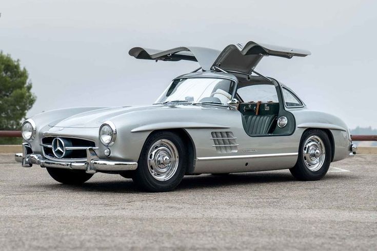 Classic silver sports car with gullwing doors open, parked on outdoor pavement. Iconic vintage design, perfect for auto enthusiasts.