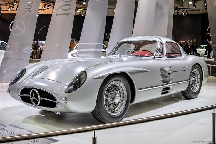 Classic silver vintage sports car on display, featuring sleek curves and a Mercedes-Benz logo, showcased at an auto show.