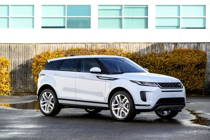 Sleek white SUV parked in an urban setting, showcasing modern design and luxury against a backdrop of windows and autumn foliage.