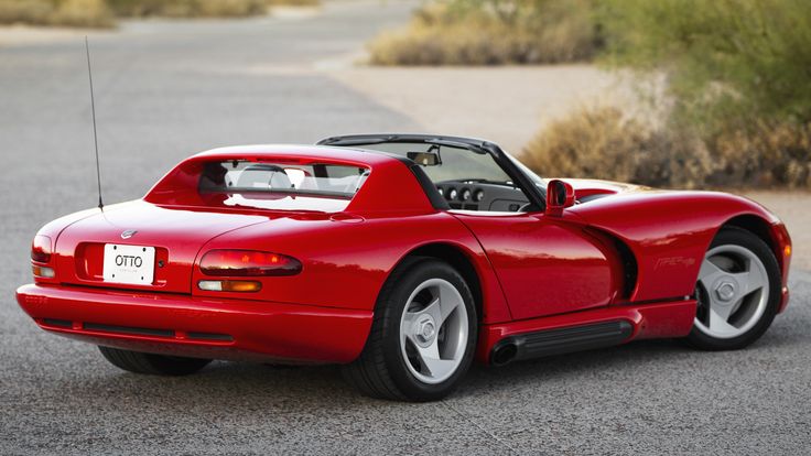 Red convertible sports car parked on a scenic road, showcasing sleek design and shiny alloy wheels. Summer driving vibes.