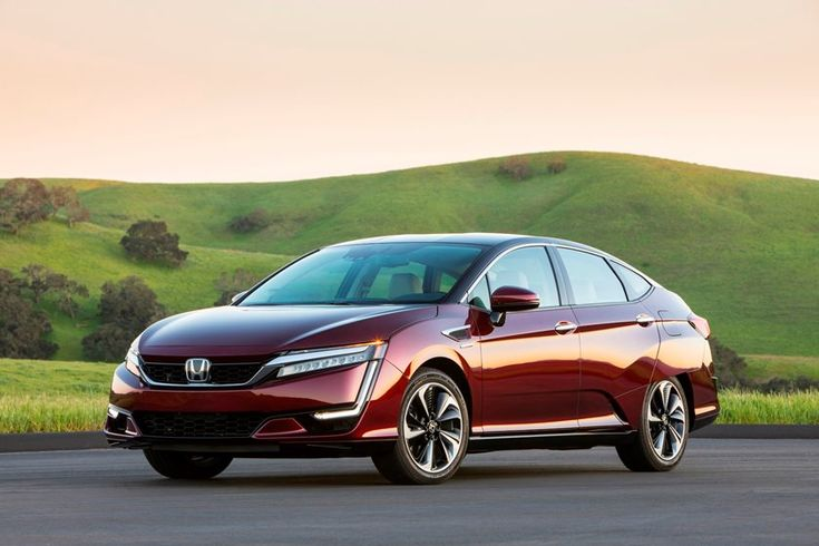 Red Honda sedan parked in a scenic green landscape with hills, showcasing its modern design and sleek features.