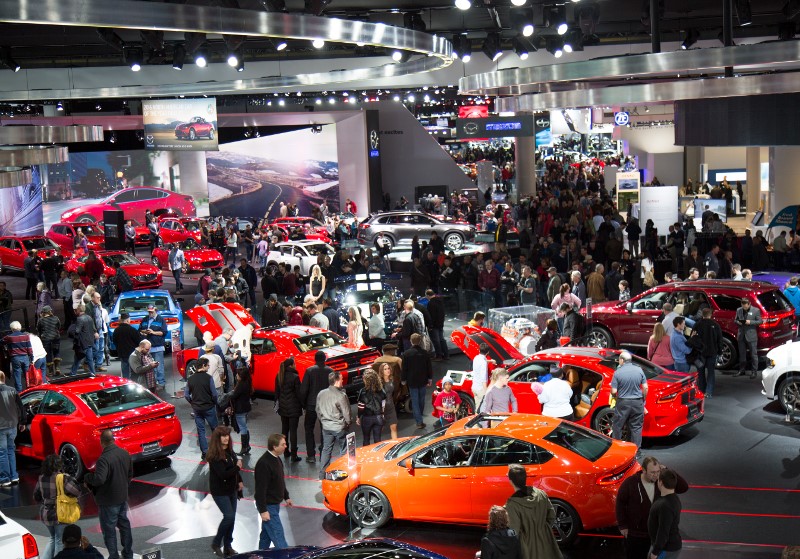 Busy car show floor featuring vibrant new models and a crowd of excited attendees exploring the latest automotive innovations.