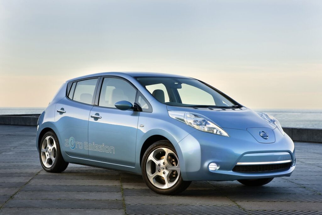 nissan-leaf-exterior-24kwh-2010-hevcars-01 - Engine Stories Blue electric car parked on a scenic oceanside pavement, promoting zero emissions for sustainable transport.