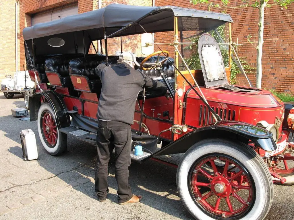 unnamed - Engine Stories Mechanic working on a vintage red car with a black canopy, showcasing classic automotive design in a sunny setting.