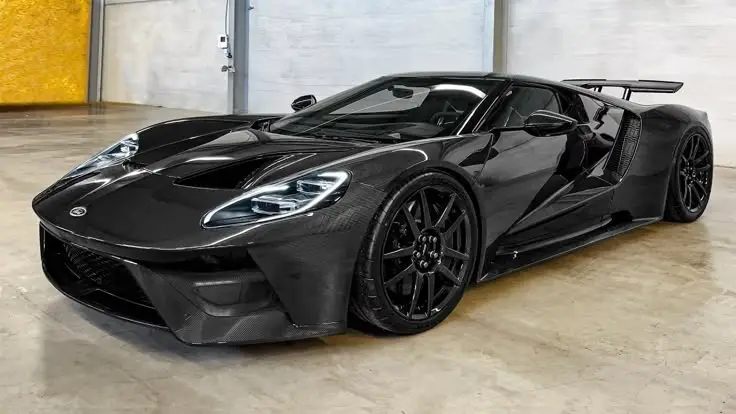 Sleek black sports car with aerodynamic design and carbon fiber body, parked indoors on a concrete floor.