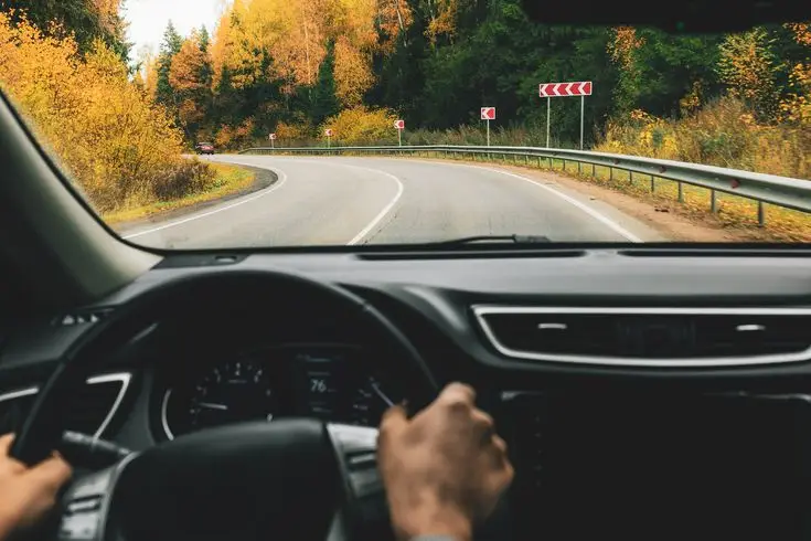 Driver navigating through a scenic autumn road with colorful foliage and winding curves, view from inside the car.