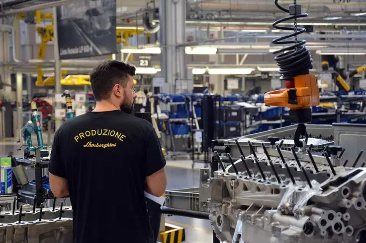 Factory worker in Lamborghini assembly line overseeing engine construction, showcasing automotive manufacturing precision and expertise.
